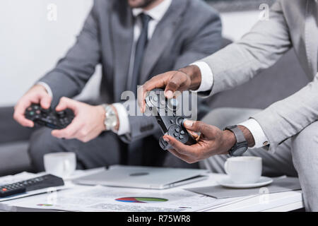 Vista ritagliata di imprenditori multietnica seduta a tavola con documenti e tenendo i gamepad Foto Stock