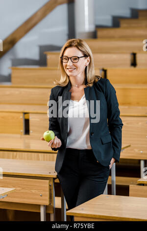 Sorridente insegnante femminile in abbigliamento formale azienda apple in aula Foto Stock