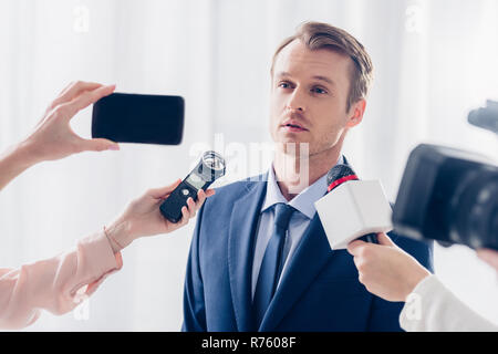 Bello imprenditore dando intervista ai giornalisti e guardando lontano in office Foto Stock