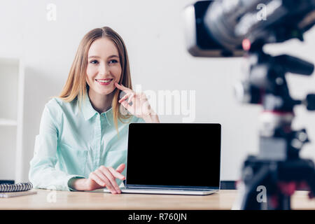 Sorridente attraente femmina registrazione freelancer vlog in ufficio, computer portatile con schermo vuoto sul piano portapaziente Foto Stock