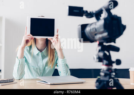 Video di sesso femminile di blogger vlog di registrazione e che ricopre la faccia con il tablet con schermo vuoto in ufficio Foto Stock