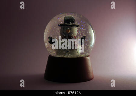 Questo pupazzo di neve in una cupola di vetro è circondato da fiocchi di neve turbinano intorno come una tempesta di neve. Isolato su sfondo rosa. Foto Stock
