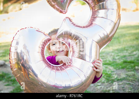 Carino Bambina giocando con il numero tre del palloncino in Mylar all'esterno. Foto Stock