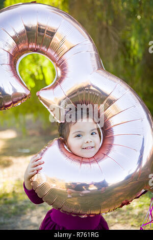 Carino Bambina giocando con il numero tre del palloncino in Mylar all'esterno. Foto Stock