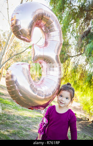 Carino Bambina giocando con il numero tre del palloncino in Mylar all'esterno. Foto Stock