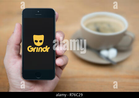 Un uomo guarda al suo iPhone che visualizza il logo Grindr (solo uso editoriale). Foto Stock