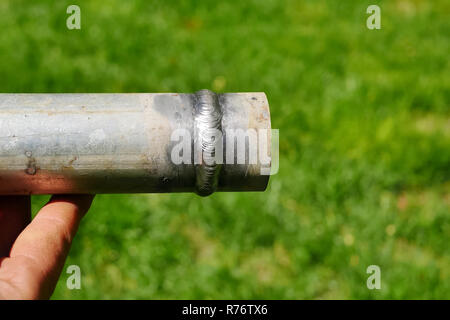 Tubo metallico con un giunto saldato nella mano di un saldatore è l'uomo. Foto Stock