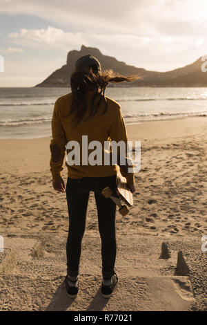 Donna in piedi con lo skateboard sulla spiaggia Foto Stock
