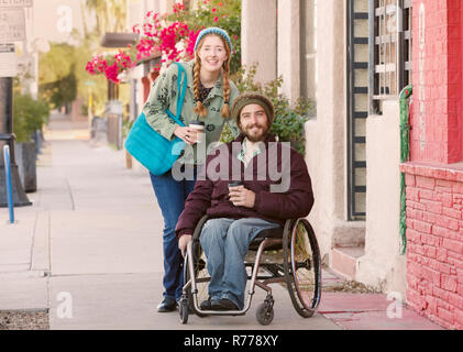 Donna che indossa vestito blu e uomo in sedia a rotelle Foto Stock