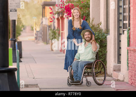 Donna che indossa vestito blu e uomo in sedia a rotelle Foto Stock