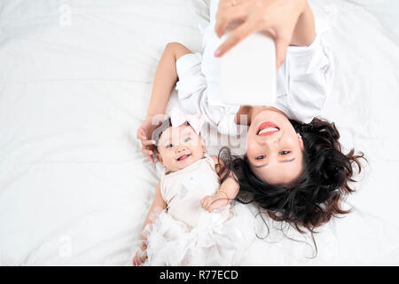 Una donna con un bambino facendo un selfie sdraiato sul pavimento in legno Foto Stock