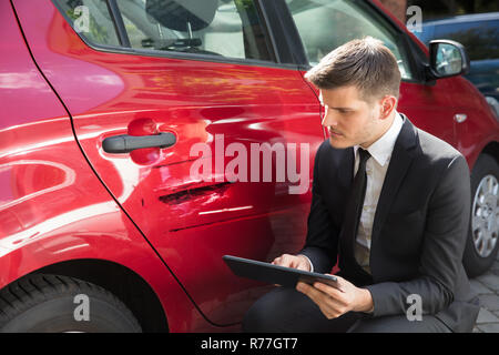 Uomo di assicurazione di riempimento forma vicino auto danneggiata Foto Stock