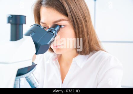 Scienziato analizzando vetrino del microscopio in laboratorio. Giovane donna tecnico sta esaminando un campione istologico, una biopsia in laboratorio di cancro ri Foto Stock