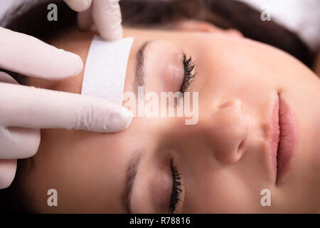 Close-up del medico la mano ceretta donna di fronte con la striscia di cera Foto Stock