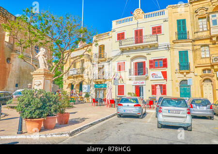 NAXXAR, Malta - 14 giugno 2018: la scenografica piazza con edifici storici con colore rosso brillante le finestre e le persiane e la caffetteria al piano terra, sul ju Foto Stock