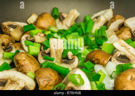 Close-up di verdi tritate le cipolline e i funghi commestibili in una padella. Foto Stock