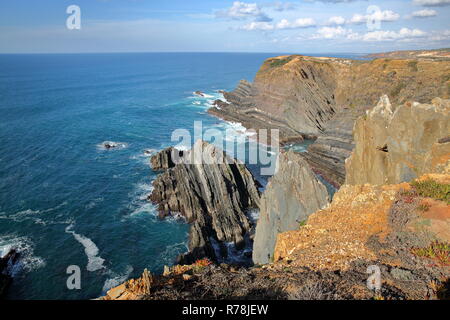 Drammatica e scogli colorati sul Alentejo West Coast a Cabo Sardao, Alentejo, Portogallo, con cicogne bianche nidificanti nella parte superiore delle scogliere rocciose Foto Stock