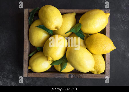 I limoni con foglie verdi nella casella su sfondo nero, vista dall'alto. Organici di agrumi freschi Limoni. Foto Stock