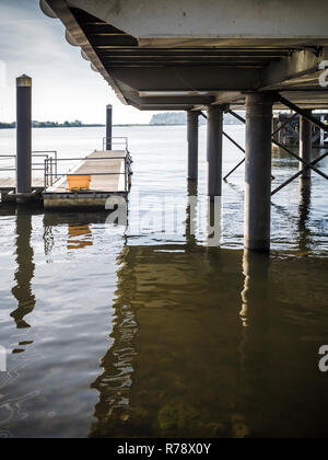 Vista sinistri di acqua increspata sotto un dock sollevata o boardwalk con riflessi della struttura di supporto. La Baia di Cardiff, Galles , REGNO UNITO Foto Stock