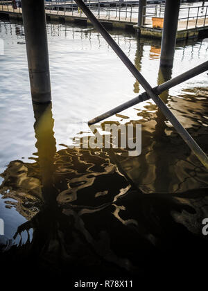 Vista sinistri di acqua increspata sotto un dock sollevata o boardwalk con riflessi della struttura di supporto. La Baia di Cardiff, Galles , REGNO UNITO Foto Stock