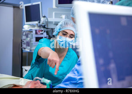 Medico donna in chirurgia operanti stanza di ospedale esegue un'operazione. Chirurgo medic nel lavoro di protezione indossare guanti, maschera e cappuccio Foto Stock