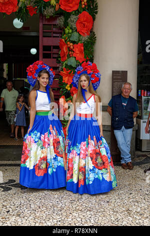 Due giovani donne nelle versioni colorate del costume tradizionale con ampie gonne pieghettate e fiorito di testate nella città di Funchal in Madeira Foto Stock