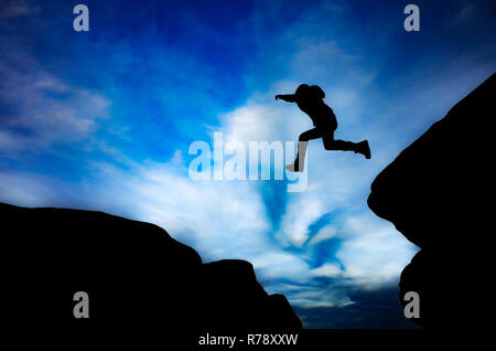 Silhouette di boy il salto tra le rocce Foto Stock