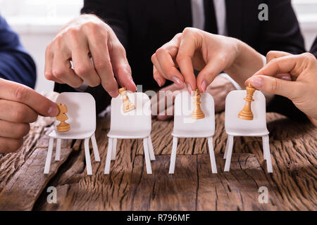 Businesspersons le mani ponendo le figure di scacchi su sedie Foto Stock