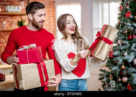 Ritratto di una giovane coppia adorabile in maglioni in piedi insieme con il nuovo anno doni vicino all'albero di Natale a casa Foto Stock