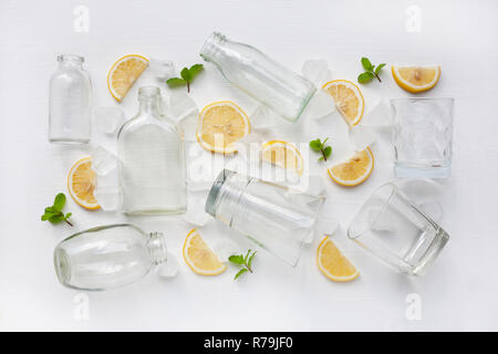 Bicchieri e bottiglie per bevande con le fette di limone, menta e ghiaccio su Foto Stock