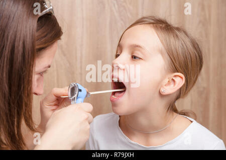 Femmina pediatra o medico esamina età elementari della ragazza utilizzando gola abbassa lingua di legno e la torcia. Bambino examinat fisico Foto Stock