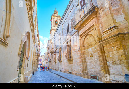 MDINA, Malta - 14 giugno 2018: le alte pareti di edifici medievali della fortezza e la torre campanaria della chiesa dell'Annunciazione, il 14 giugno in Mdina. Foto Stock