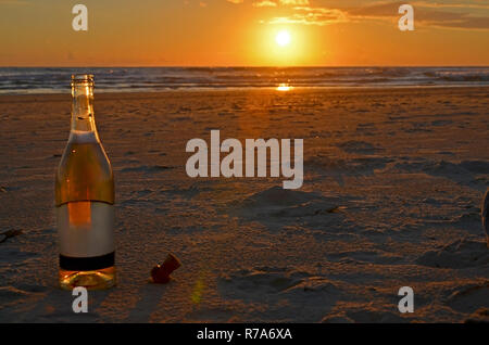 Aprire una bottiglia di champagne si erge con un tappo di sughero sulla sabbia. Riunione del tramonto sul mare mediterraneo in Israele. Foto Stock
