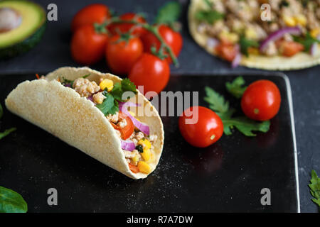 Mexican tacos con carne di maiale, spezie e verdure su una pietra nera piastra su uno sfondo scuro con ingredienti per tacos e Menu ristorante concetto. Foto Stock