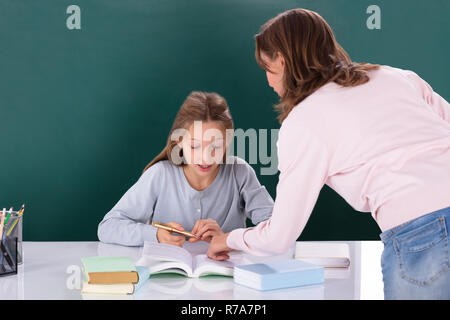 Insegnante femminile aiutando il suo studente facendo il lavoro in classe in aula Foto Stock