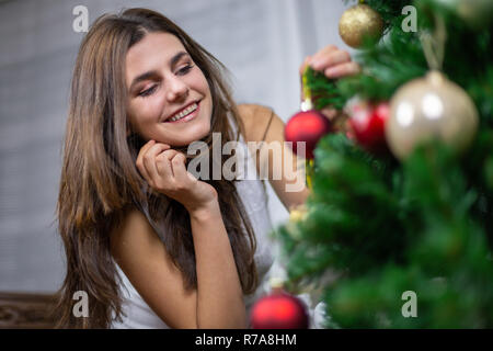 Bella giovane donna sorridente e appendere piccola pallina su albero di Natale Foto Stock