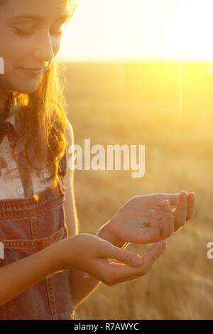 Teen ragazza tiene in mano i chicchi di grano in tempo al tramonto Foto Stock