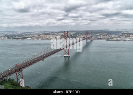 Famoso XXV Aprile del ponte sul fiume Tago a Lisbona, Portogallo in un giorno nuvoloso. Vista aerea da sinistra (sud) banca del fiume Tago. Foto Stock