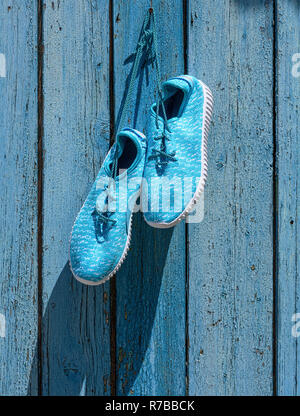 Sneakers tessile appendere su un chiodo contro lo sfondo di colore blu schede vecchia Foto Stock