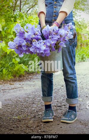 Ragazza con un secchio in giardino con iridi Foto Stock