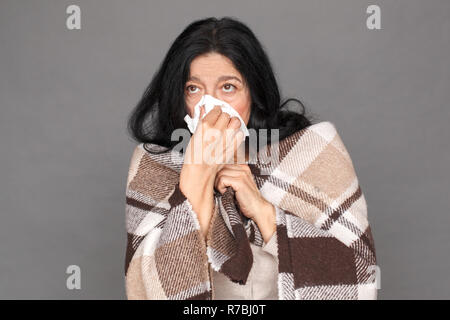 Freestyle. Signora matura in plaid coperta isolato permanente su grigio soffia il naso nel tessuto close-up Foto Stock
