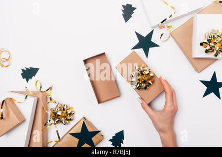 Donna si apre a mano dono tra piatto telaio laici di decorazioni di Natale, scatole, oro fiocchi e nastri, carta nera-cut stelle su fondo bianco, parte superiore vi Foto Stock