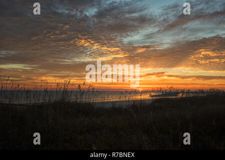 Majestic Sun pigoli oltre l'orizzonte in riva al mare, incorniciato da marsh, mare di avena, e incredibili nuvole riflettono nell'oceano. Foto Stock