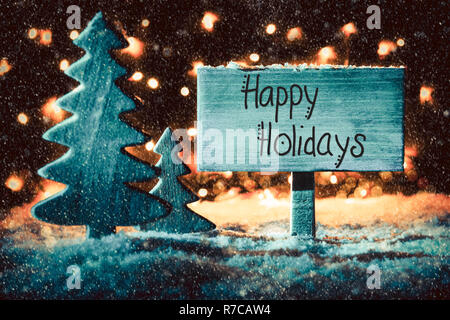 Cartello in legno con la calligrafia Inglese Buone Vacanze. Albero di Natale sulla neve e le luci fairy in background. Spotlight blu Foto Stock