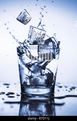 Splash di cubetti di ghiaccio in un bicchiere di acqua Foto Stock