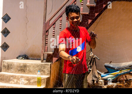 Don Daeng, Laos - Aprile 27, 2018: pescatore locale la riparazione di una rete da pesca nel cortile della sua casa in una zona rurale remota del Laos Foto Stock