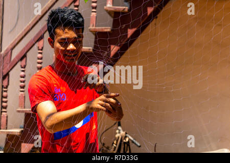 Don Daeng, Laos - Aprile 27, 2018: pescatore locale la riparazione di una rete da pesca nel cortile della sua casa in una zona rurale remota del Laos Foto Stock