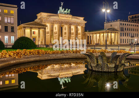 La famosa Porta di Brandeburgo a Berlino di notte, che si riflette in una fontana Foto Stock