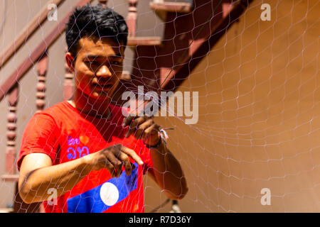 Don Daeng, Laos - Aprile 27, 2018: pescatore locale la riparazione di una rete da pesca nel cortile della sua casa in una zona rurale remota del Laos Foto Stock