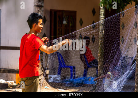 Don Daeng, Laos - Aprile 27, 2018: pescatore locale la riparazione di una rete da pesca nel cortile della sua casa in una zona rurale remota del Laos Foto Stock